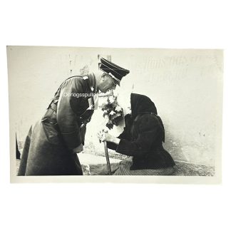 Rare original World War II-era photograph of Dr. Arthur Seyss-Inquart, high-ranking Austrian Nazi official and Reich Commissioner for the occupied Netherlands, engaging with an elderly woman dressed in traditional attire. Captured in a candid and unusual moment of public interaction, this image offers strong historical and collector value due to its depiction of a prominent Nazi figure in a non-ceremonial context. Ideal for collectors specializing in Third Reich political figures or occupation-era visual documentation.