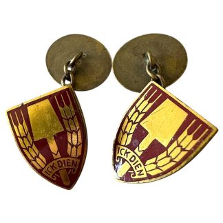 Cufflinks from the Dutch Labour Service (NAD) during World War II, featuring the emblem of a yellow spade flanked by wheat stalks on a red shield, with the motto 'ICK DIEN' ('I serve').