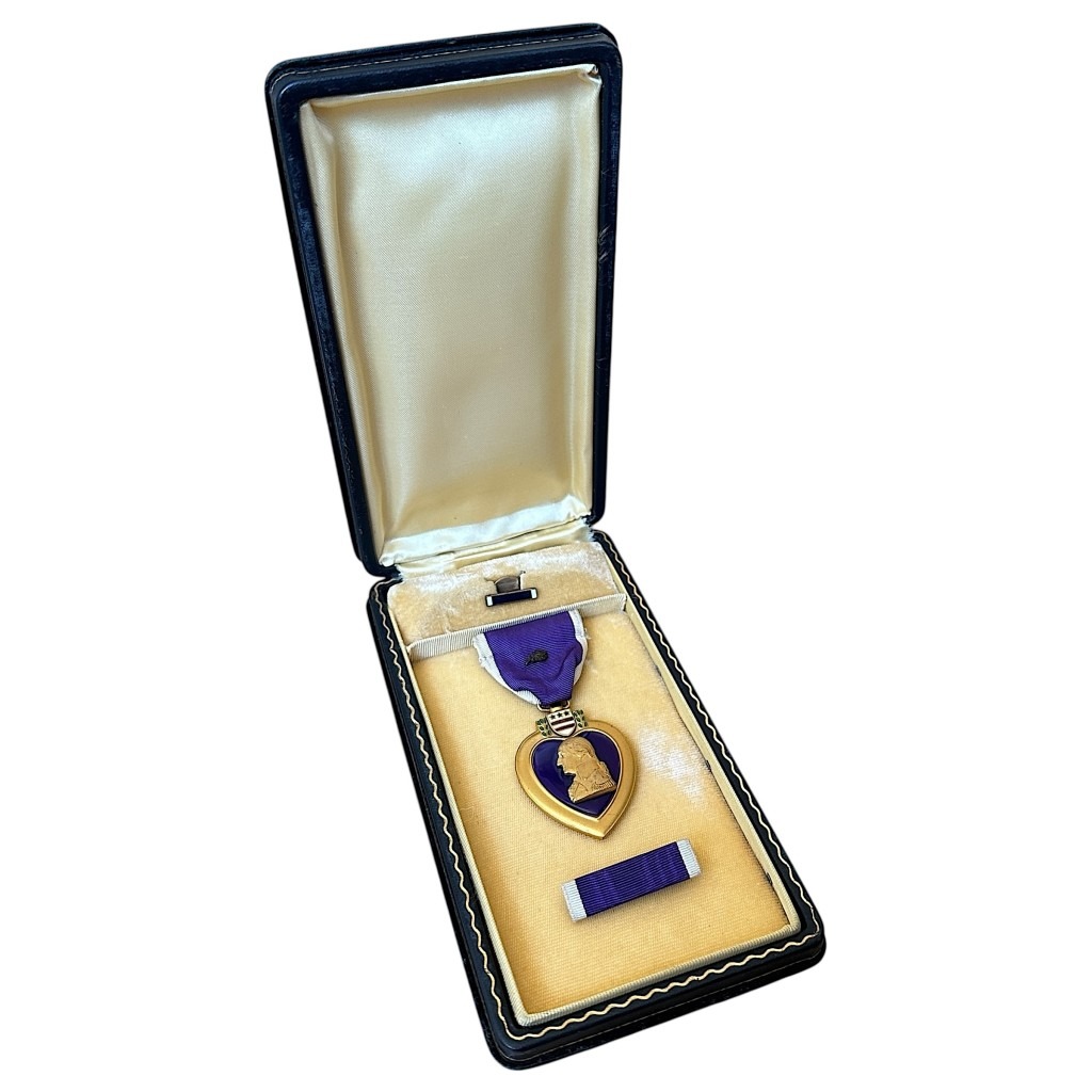 Original WWII U.S. Purple Heart medal displayed in its open presentation case, featuring the medal with a purple ribbon and gold heart-shaped pendant bearing the profile of George Washington. Also included are the matching ribbon bar and buttonhole pin.