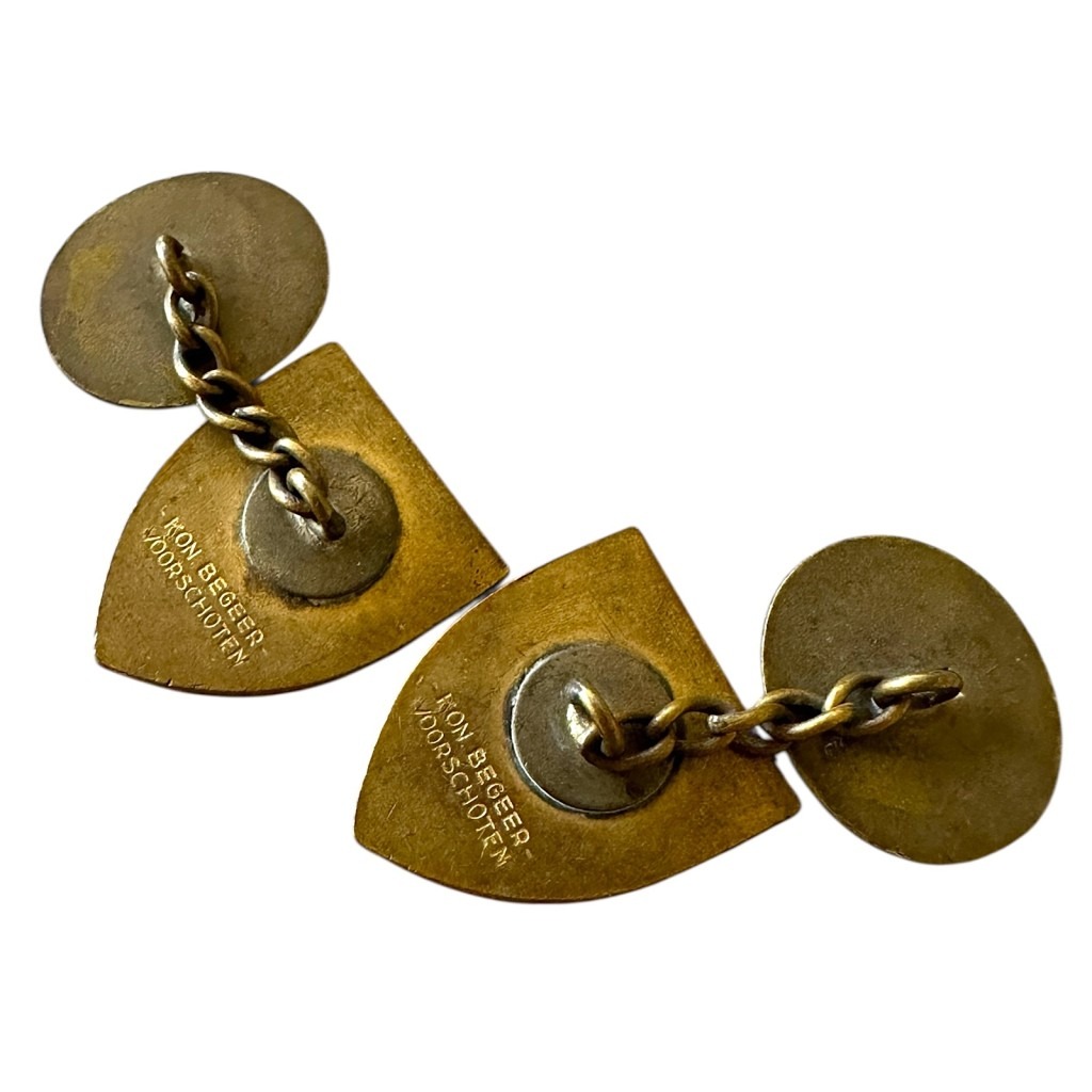 Cufflinks from the Dutch Labour Service (NAD) during World War II, featuring the emblem of a yellow spade flanked by wheat stalks on a red shield, with the motto 'ICK DIEN' ('I serve').