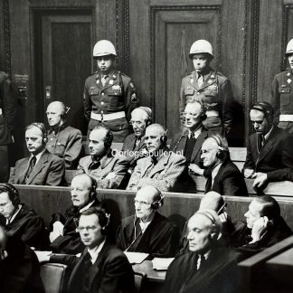 Original British press photo of the Nuremberg Trials in 1946, showing Nazi war criminals in the defendants’ dock wearing headphones for translation, guarded by American military police. Visible are leading figures such as Rosenberg, Frank, Frick, Streicher, Funk, Papen, Speer, Seyss-Inquart, and von Neurath during the International Military Tribunal after World War II.