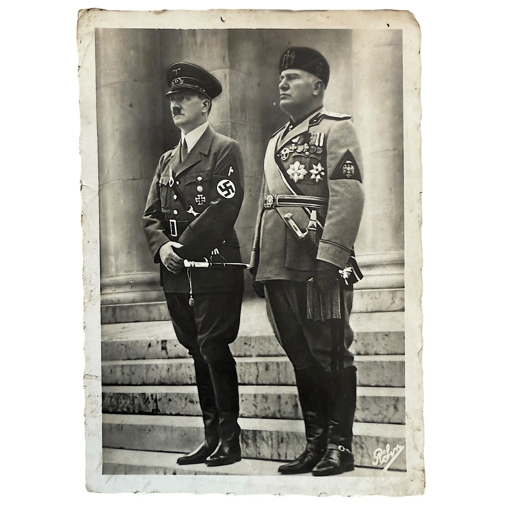 Cartolina storica in bianco e nero che ritrae Adolf Hitler e Benito Mussolini in uniforme militare, in piedi su una scalinata di pietra. Hitler indossa l’uniforme del partito nazista con fascia al braccio e croce di ferro, Mussolini indossa l’uniforme militare italiana con decorazioni e medaglie. Fotografia d’epoca dell’era fascista e nazista.