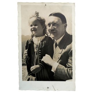 Historic black-and-white postcard showing Adolf Hitler with a young girl in traditional dress, outdoors at the Obersalzberg. The child is smiling while Hitler stands close beside her. Period photograph from the Nazi era.
