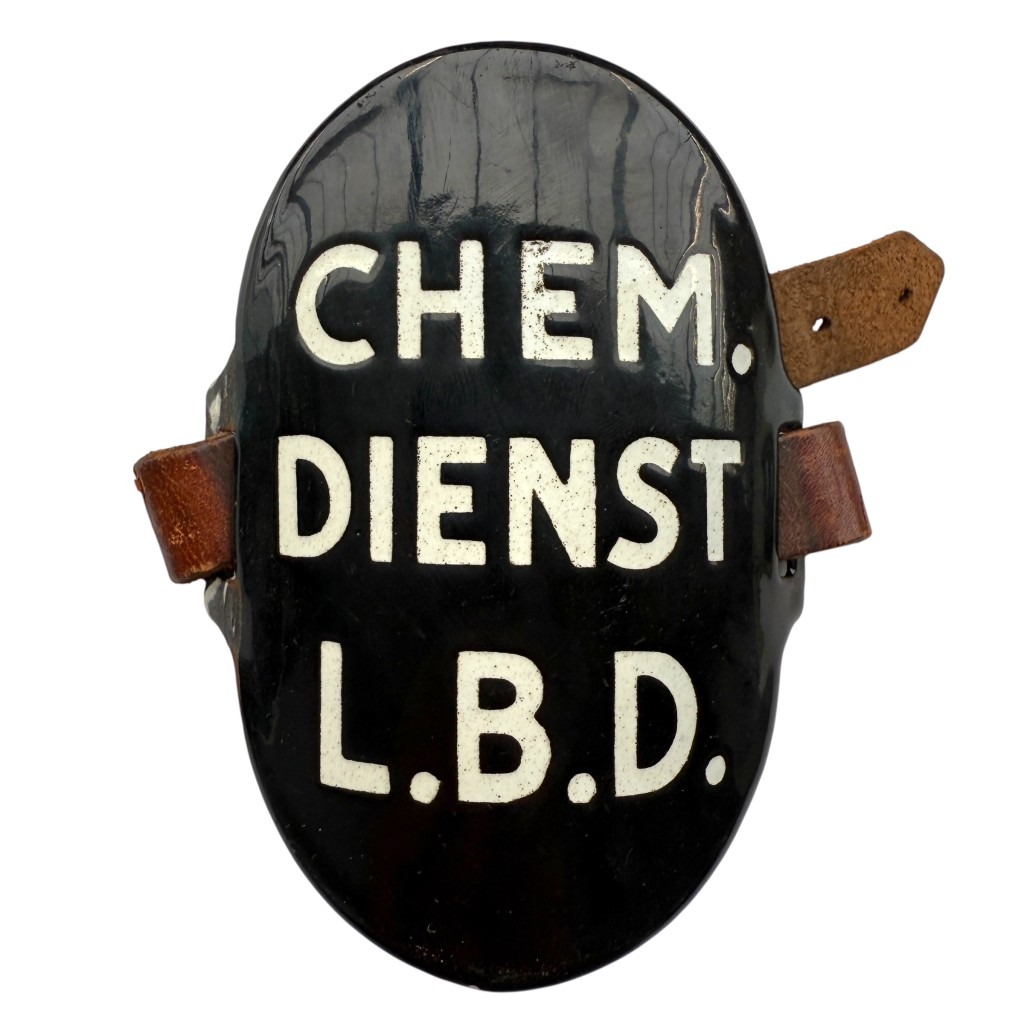 Zwart geëmailleerd armbandschildje met witte letters 'CHEM. DIENST L.B.D.' en leren riempjes, gebruikt door de Chemische Dienst van de Luchtbeschermingsdienst in Nederland tijdens de Tweede Wereldoorlog.