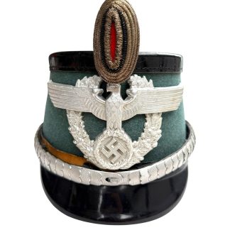 Original WWII German Schutzpolizei Officer’s Tschako helmet by Erel, police green felt with silver eagle, wreath and swastika insignia, complete with officer’s aluminum chin scales – rare authentic Ordnungspolizei headgear collectible.