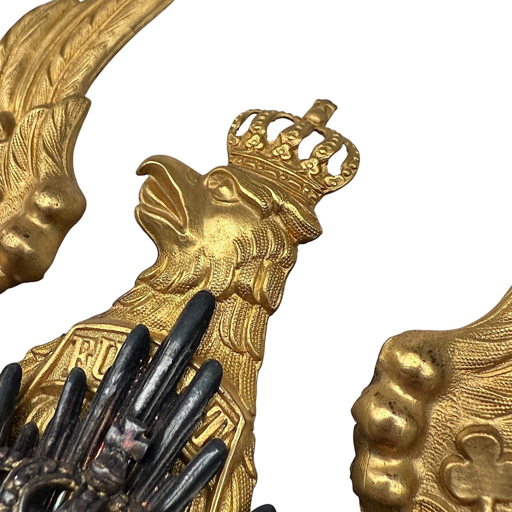 Close-up of an original WW1 German Prussian Pickelhaube helmet plate showing the crowned Prussian eagle with detailed feather engraving and gilt finish.