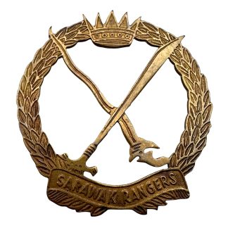 Original Malay Sarawak Rangers cap badge from the 1950s, brass cap badge with crossed parang-style blades within a laurel wreath, surmounted by a crown and bearing the scroll “Sarawak Rangers,” post-war military insignia from the Malayan Emergency, collectible for British and colonial military insignia collectors.