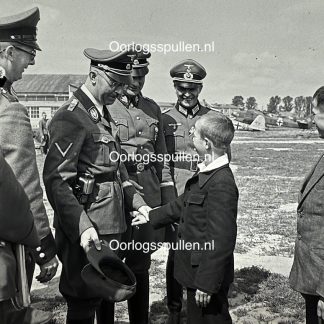 Original WWII German photo positive of Reichsführer-SS Heinrich Himmler shaking hands with a young boy at an airfield, rare unpublished Third Reich aviation and SS photograph for WWII photo collectors.