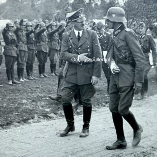 Oryginalna niemiecka fotografia z II wojny światowej w formacie pocztówkowym, przedstawiająca Adolfa Hitlera podczas inspekcji wojskowej w okupowanej Polsce. Hitler idzie wzdłuż szeregu żołnierzy Wehrmachtu, w towarzystwie wysokiego rangą niemieckiego generała. Historyczne zdjęcie kolekcjonerskie z okresu 1939–1945, militaria, autentyczna fotografia archiwalna dla kolekcjonerów i muzeów.