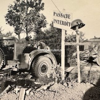 WWII France photo of German military vehicles beside “Passage Interdit” sign with shrapnel-damaged German helmet on wooden cross, original 9 x 6 cm World War II battlefield photograph collectible for France 1940–1944 collectors.