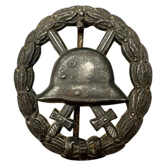 Original German WW1 wound badge black steel helmet crossed swords laurel wreath military award collectible.